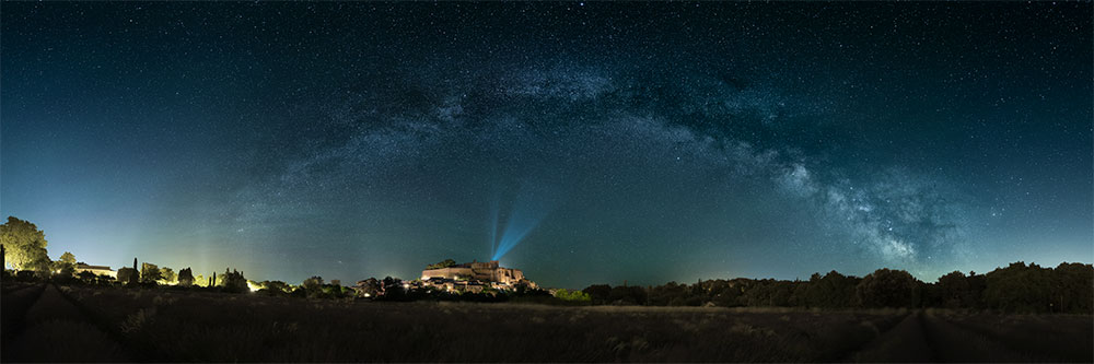 Le château de Grignan sous l'arche de la Voie lactée au-dessus d'un champ de lavande en fleurs, photographié de nuit par Vincent Eysséric.